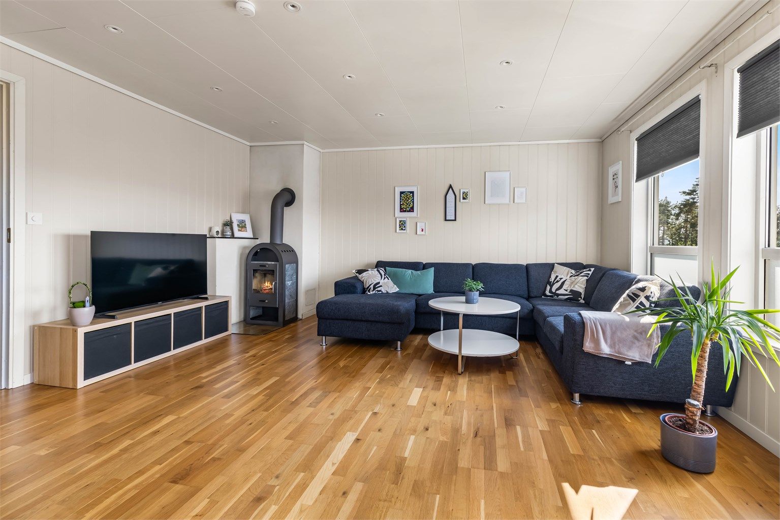 Lys og hyggelig stue med peisovn, downlights i taket og store vindusflater. 