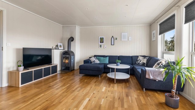 Lys og hyggelig stue med peisovn, downlights i taket og store vindusflater.