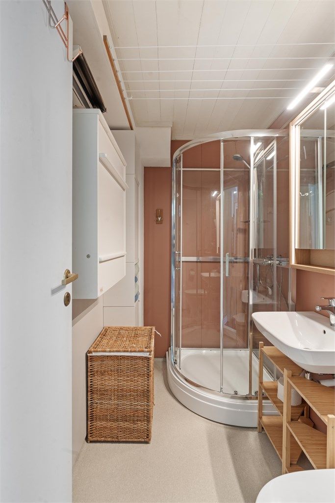 Badet er innredet med dusjkabinett, vegghengt servant og gulvstående toalett.