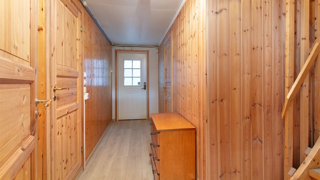 Gang i underetasjen med panelte vegger og utgang til terreng mot nord.
