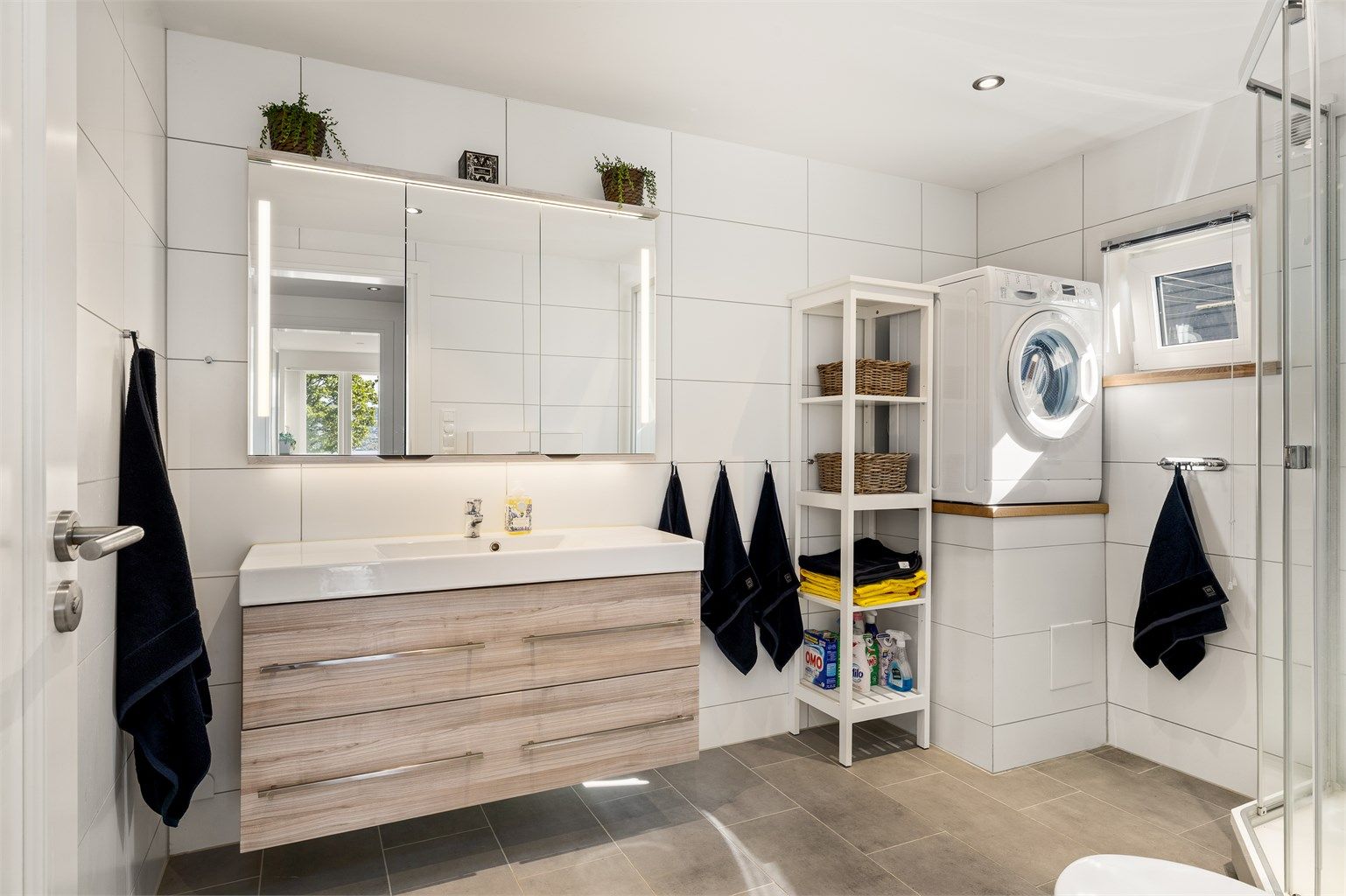 Badet har samme overlate og farge som gulvflisene i entrén, men her er det rektangulære, noe som bidrar til at rommet virker større.