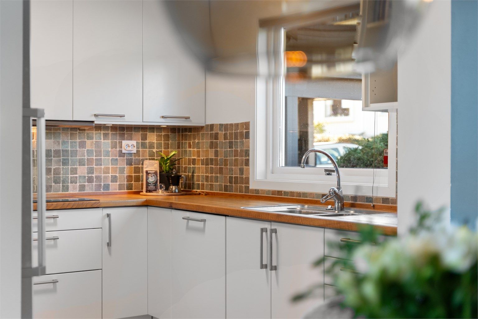 Fliser på vegg mellom overskap og benk, i tillegg til stort vindu over benk som gir lysinnslipp og utsikt mot terrasse og inngangsparti. 