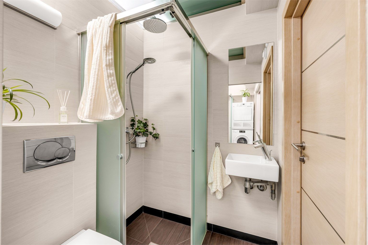 Badet nærmest gangen er innredet med vegghengt toalett og dusjnisje i frostet glass, to-greps dusjarmatur på vegg og regnfallsdusj