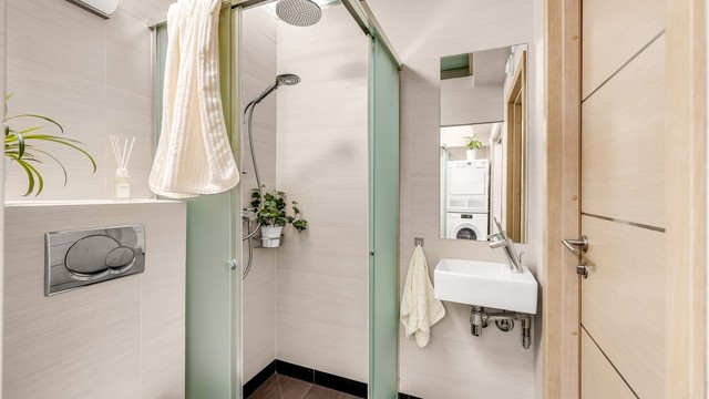 Badet nærmest gangen er innredet med vegghengt toalett og dusjnisje i frostet glass, to-greps dusjarmatur på vegg og regnfallsdusj