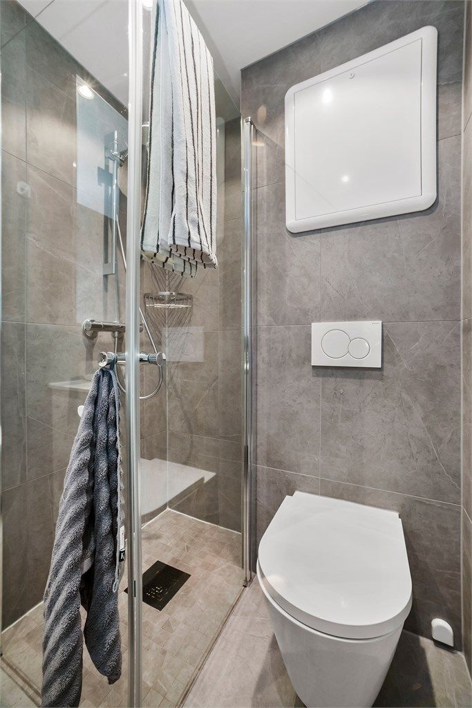 Badet har dusjhjørne med glassdører og vegghengt toalett med innebygget sisterne.