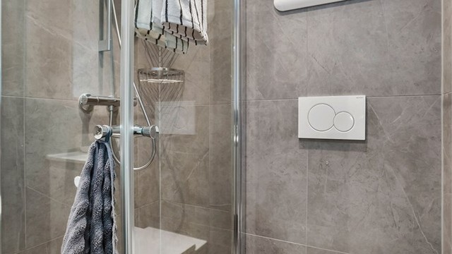Badet har dusjhjørne med glassdører og vegghengt toalett med innebygget sisterne.