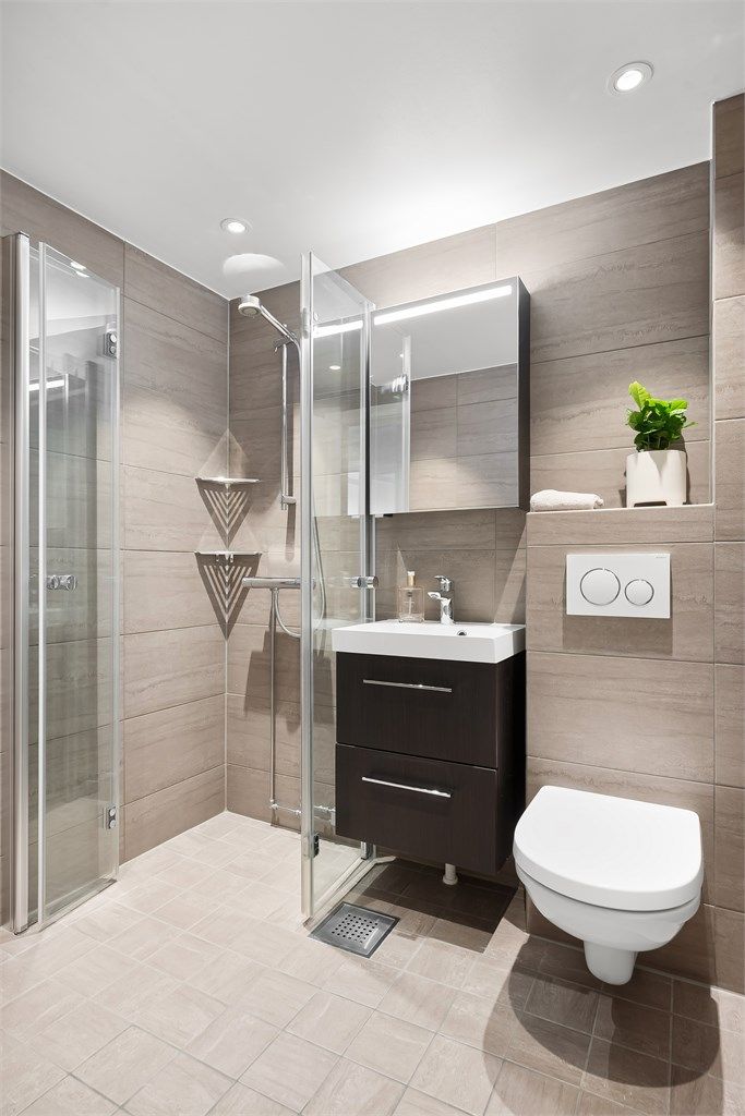 Badet er utstyrt med elektrisk gulvvarme, vegghengt toalett, servantskap med skuffeløsninger, speilskap med integrert belysning og dusjhjørne med innfellbare glassdører. Det er downlights i nedsenket himling som gir behagelig belysning.