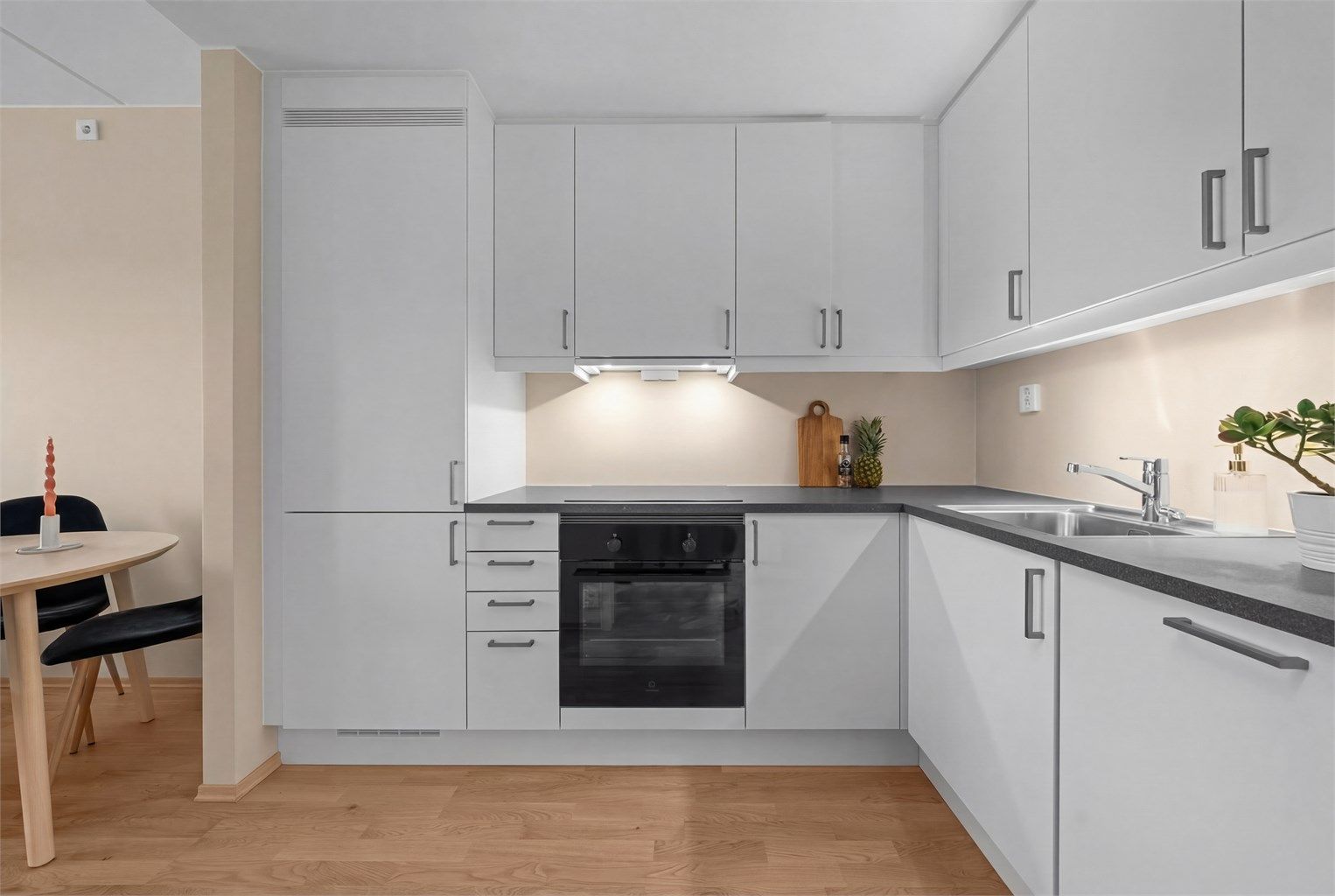 Kjøkkenet har en praktisk hjørneløsning med integrerte hvitevarer, inkludert induksjonstopp og stekeovn.