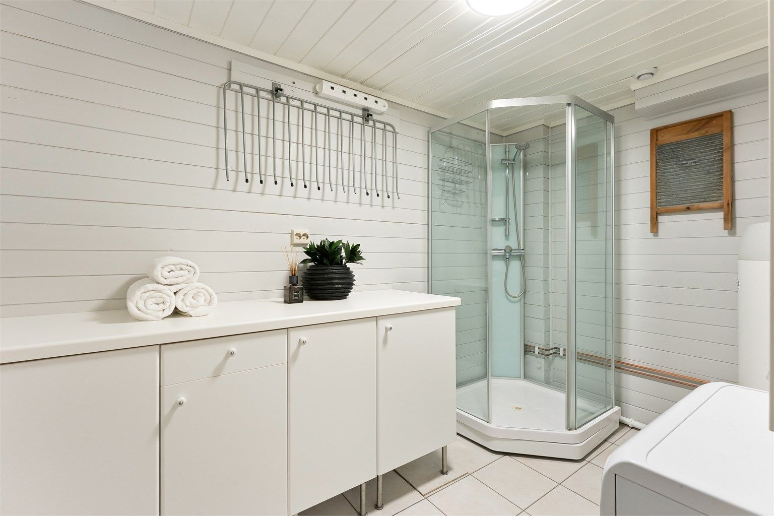 Praktisk vaskerom med flislagt gulv med gulvvarme, dusjkabinett og opplegg for vaskemaskin.