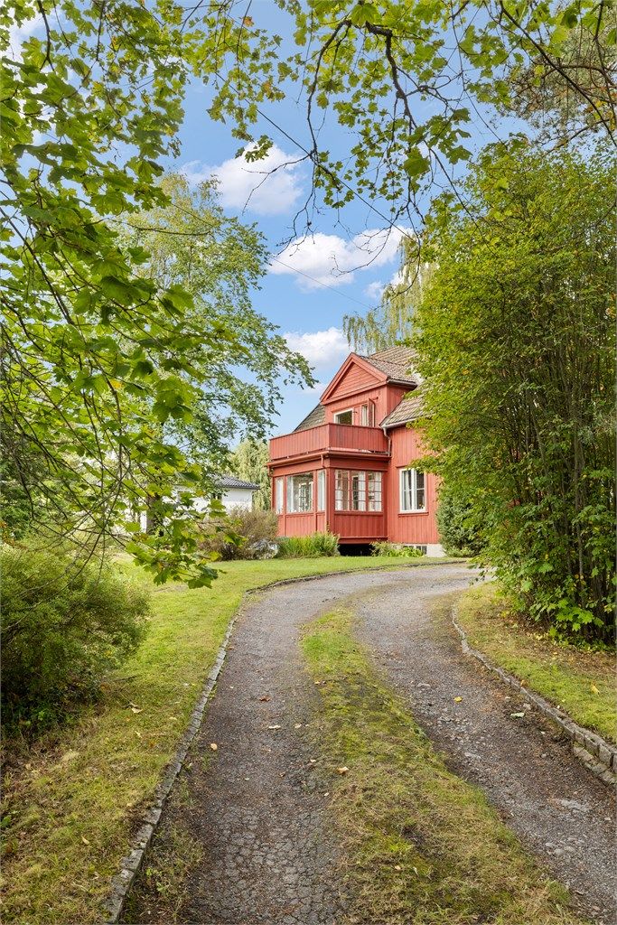 Eiendommen ligger skjermet fra veien, omgitt av frodig vegetasjon.