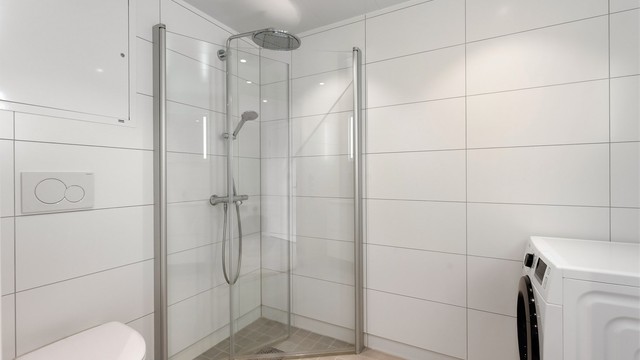 Dusjhjørne med innfellbare glassdører, regnfallsdusj og vegghengt toalett.