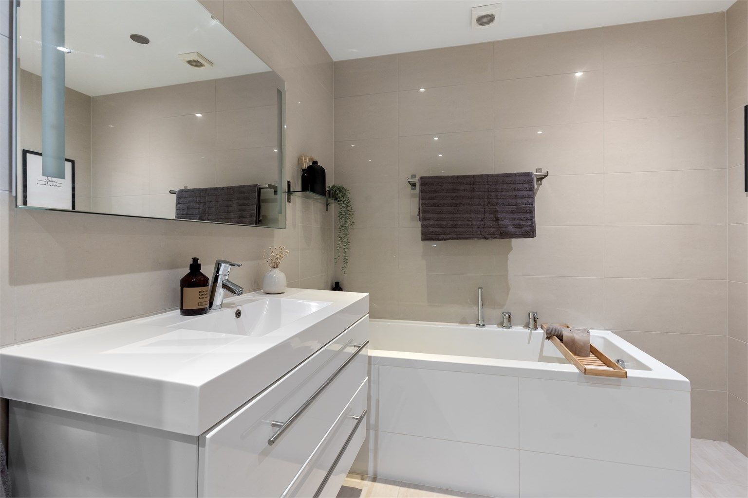 Innfliset badekar og heldekkende servant med speil og belysning.