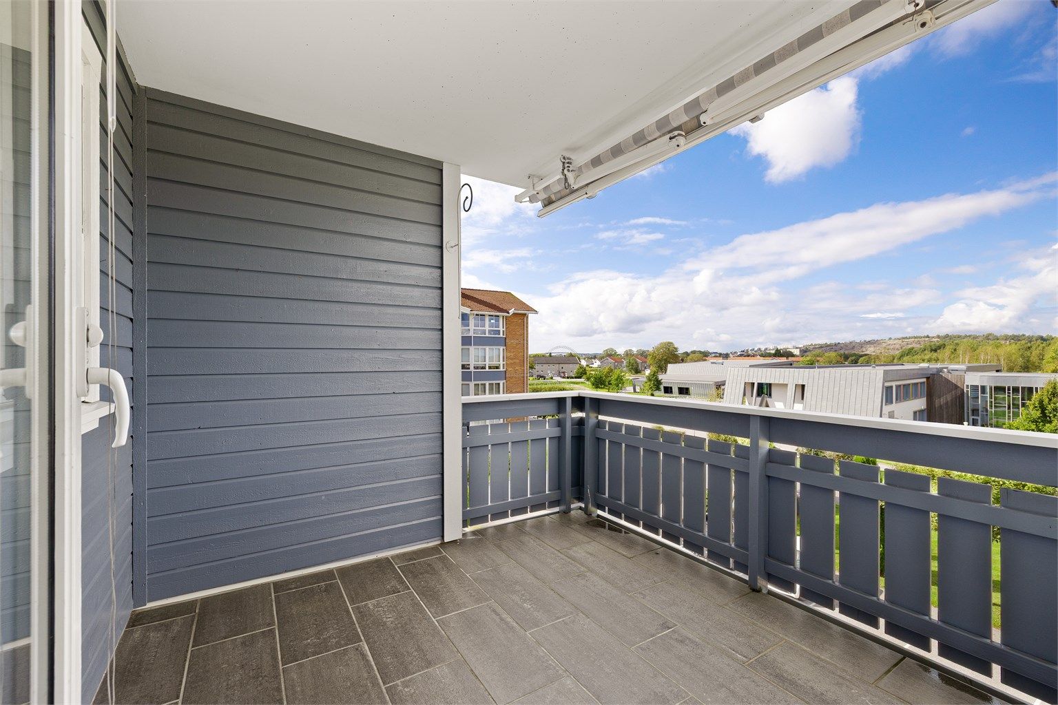 Balkongen byr på skjermet uteplass med solmarkise, flislagt gulv og utsikt mot vest.