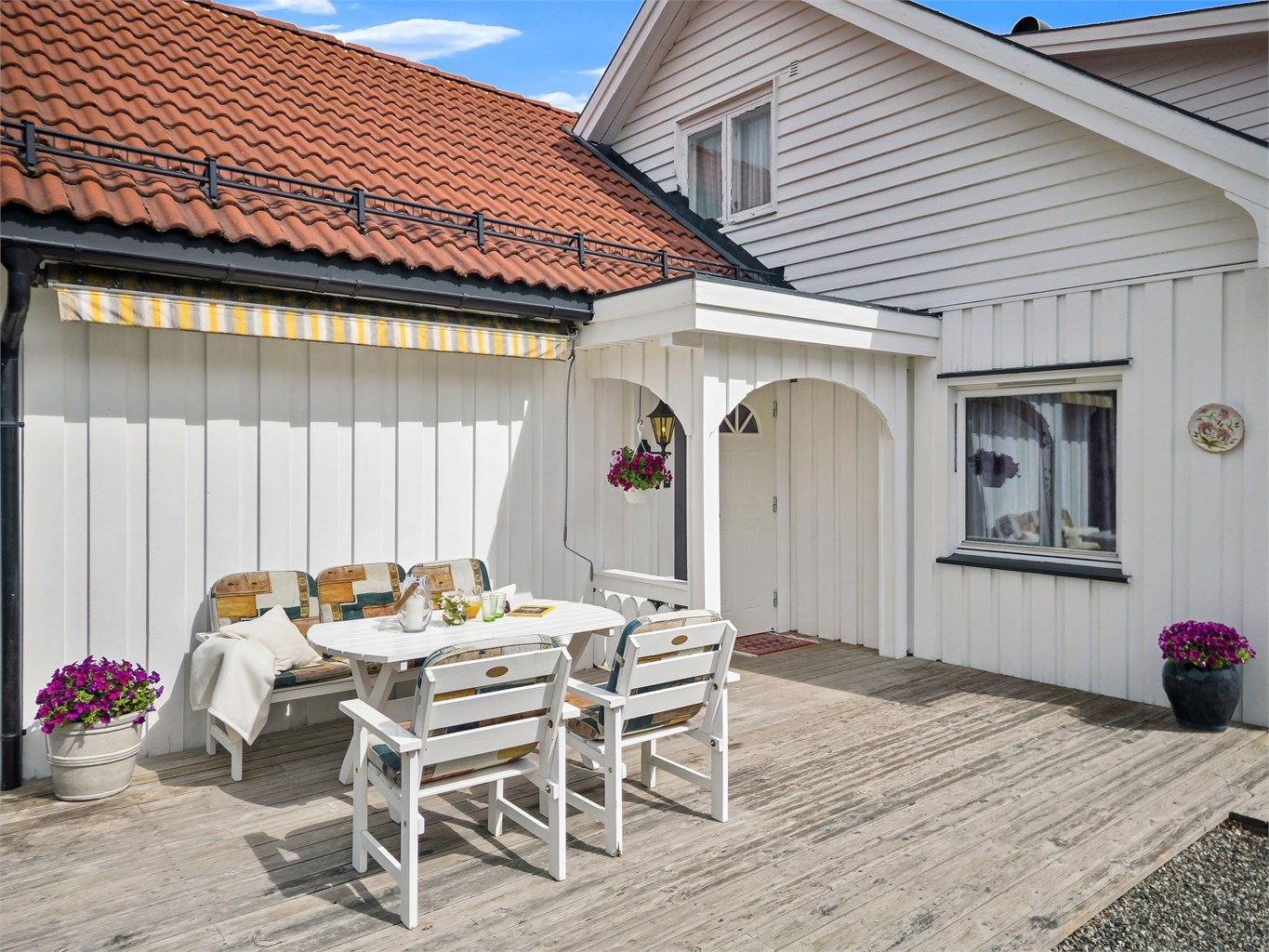 Koselig inngangsparti med fin terrasseplatting med markise og god plass til utemøbler