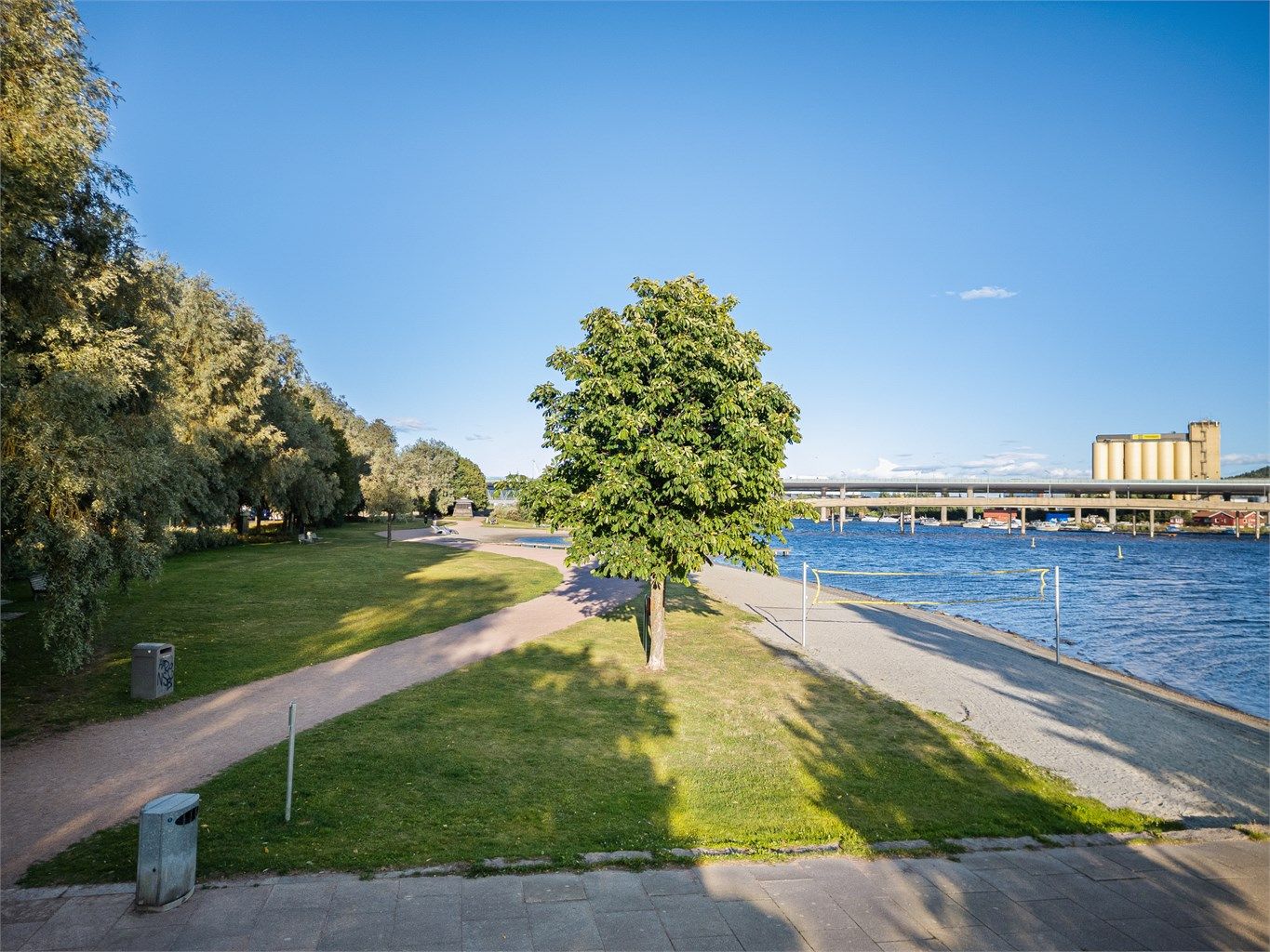 Pent opparbeidet strandpromenade med grøntområder, lekeplasser, volleyballbane og badeplass.