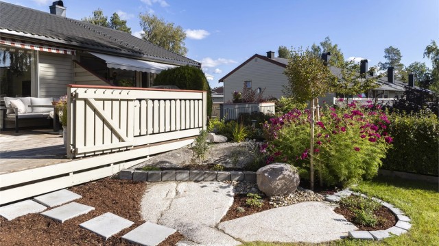 Opparbeidet hage med steinlagte tråkkheller, prydbusker og blomsterbed.
