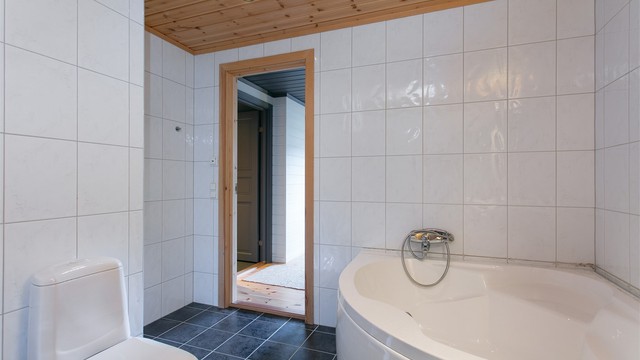 Hjørnebadekar med vegghengt armatur og panel i himlingen.