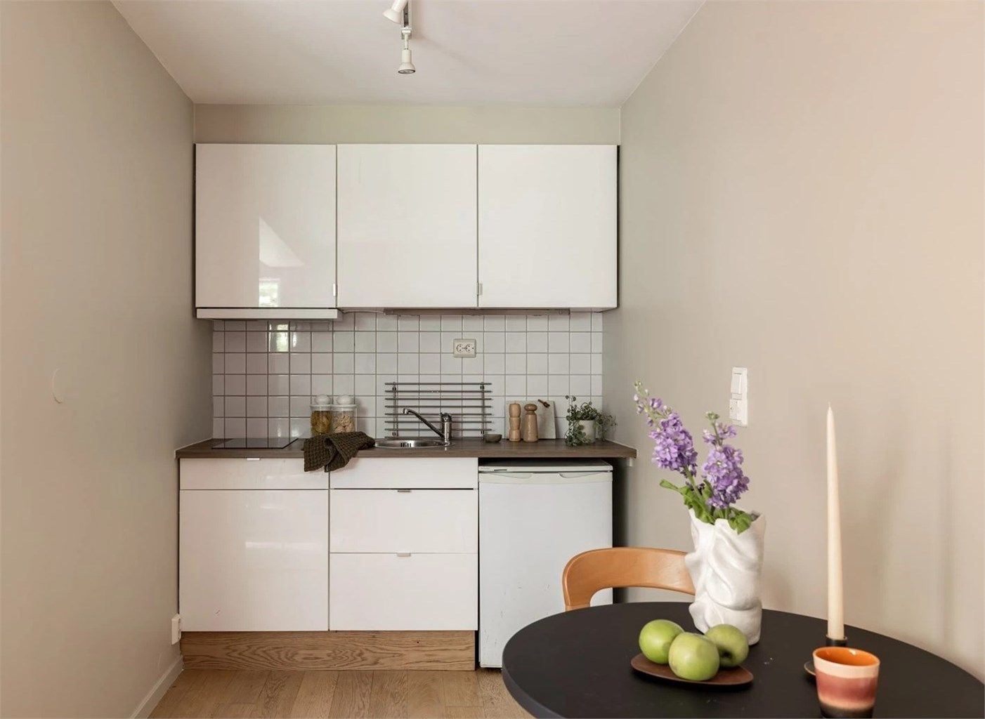 Kjøkkenet har glatte fronter, laminert benkeplate, nedfelt stålvask og fliser på vegg. Det er benkeskapsbelysning, kjøleskap og platetopp.
