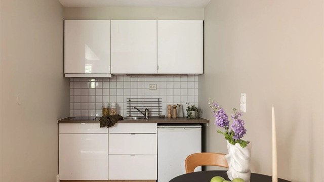 Kjøkkenet har glatte fronter, laminert benkeplate, nedfelt stålvask og fliser på vegg. Det er benkeskapsbelysning, kjøleskap og platetopp.