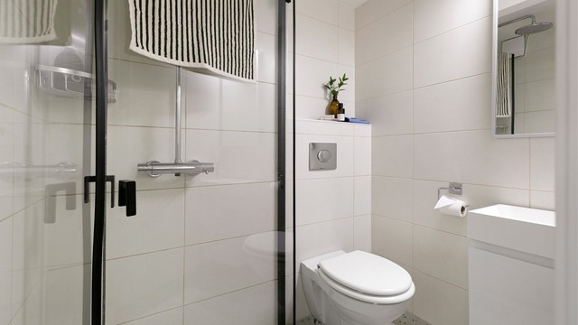 Baderom i kjeller med flislagte overflater, gulvvarme, vegghengt toalett og regndusj.