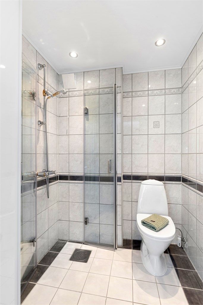 Rommet er innredet med dusjhjørne med glassdører, gulvstående toalett, servant og vegghengt speil. Nedsenket himling med downlights.