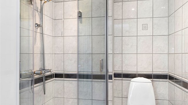 Rommet er innredet med dusjhjørne med glassdører, gulvstående toalett, servant og vegghengt speil. Nedsenket himling med downlights.