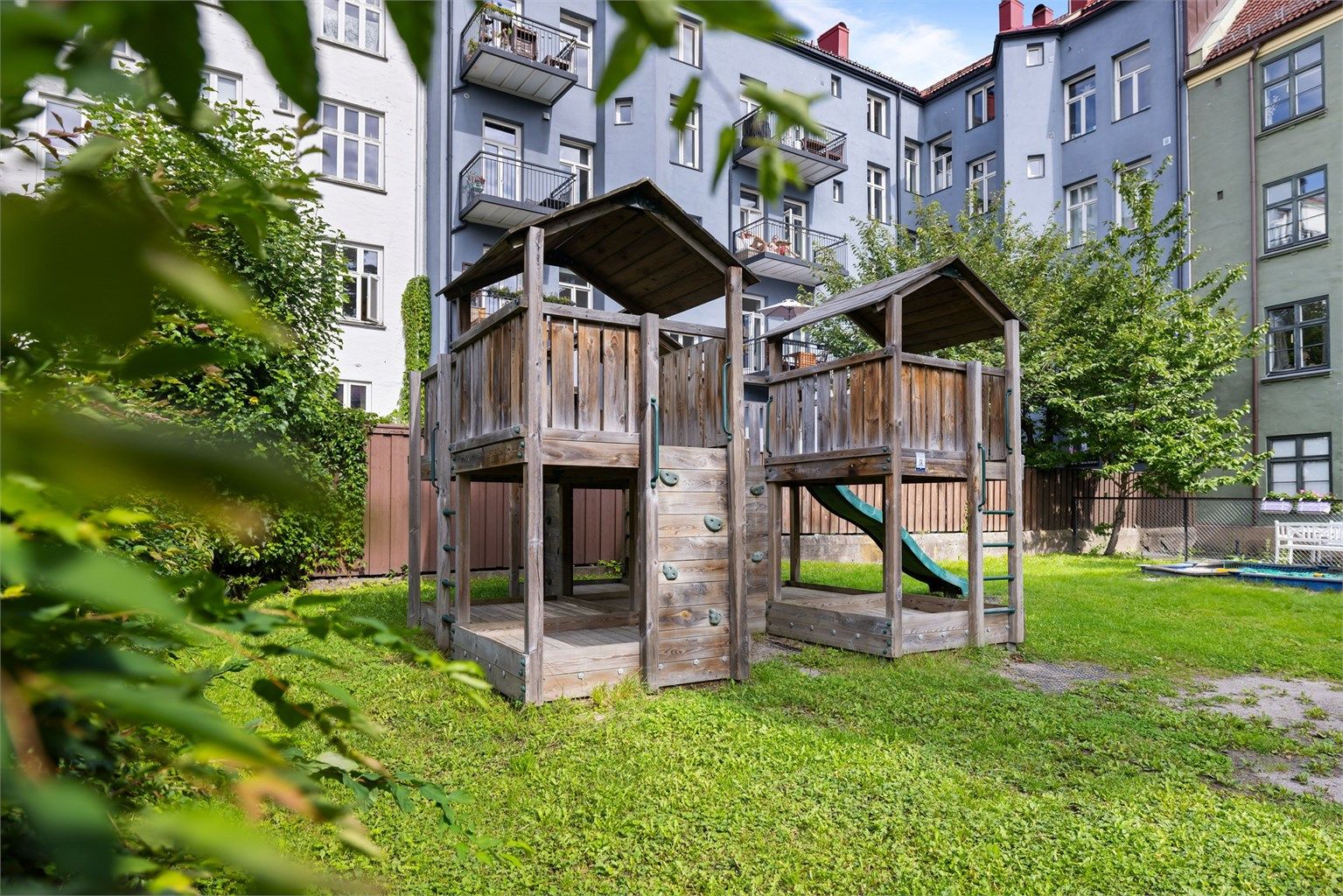 Lekeplass og bakgård med gressplen og sittebenker. Tomten er fellesareal.