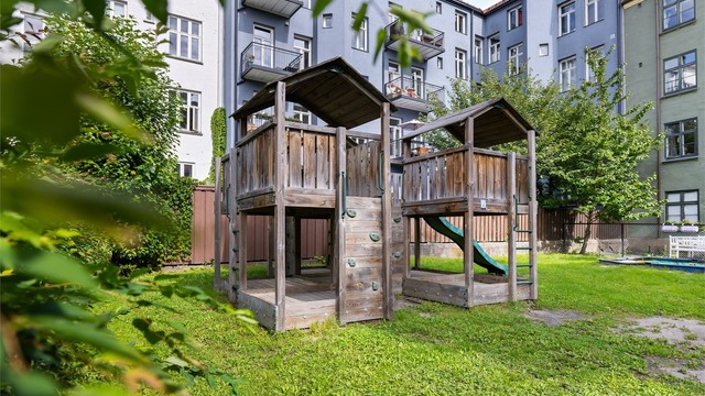 Lekeplass og bakgård med gressplen og sittebenker. Tomten er fellesareal.