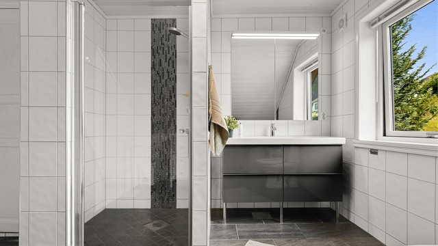 Badet er utstyrt med dusjhjørne, vegghengt servantinnredning og speilskap med overlys.