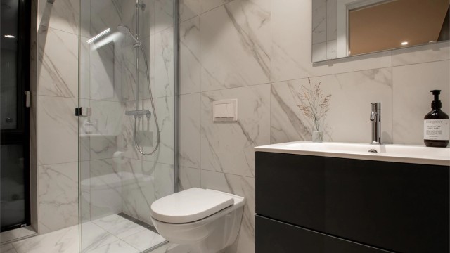 Badet har flislagte gulv og vegger, innredet med servant, vegghengt toalett og dusjhjørne.