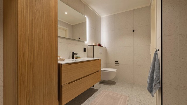 Stilrent bad i eik innredning og sorte detaljer og skyvedører som dekker vaskemaskin etc.