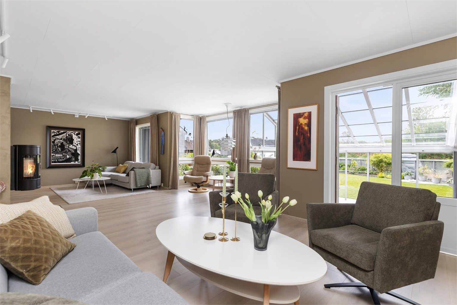 Romslig stue med peisovn og direkte utgang til en innglasset hagestue og hagen.
Foto: Marianne Lyse