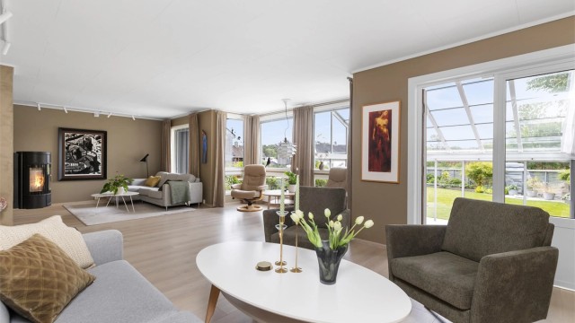 Romslig stue med peisovn og direkte utgang til en innglasset hagestue og hagen.
Foto: Marianne Lyse