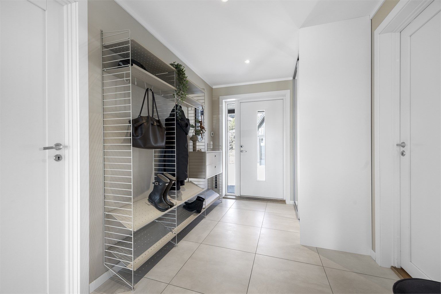 Romslig entré med flislagt gulv og god plass til garderobeløsninger, inkludert plassbygd skyvedørsgarderobe.
