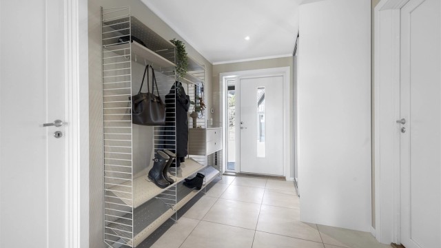 Romslig entré med flislagt gulv og god plass til garderobeløsninger, inkludert plassbygd skyvedørsgarderobe.