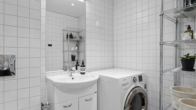 Lyst og tidløst bad med flislagte overflater og opplegg for vaskemaskin – praktisk tilrettelagt for en enkel hverdag.