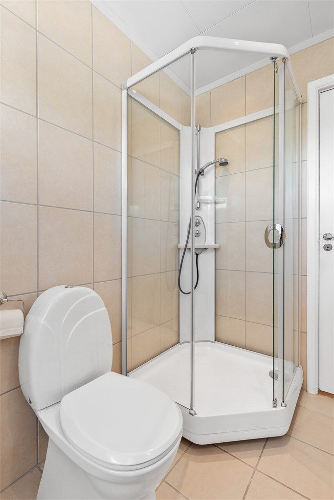 Badet har vegghengt servantinnredning med ovenpåliggende servant med armatur og speilskap med overlys. Dusjkabinett med dusjarmatur og gulvstående toalett.