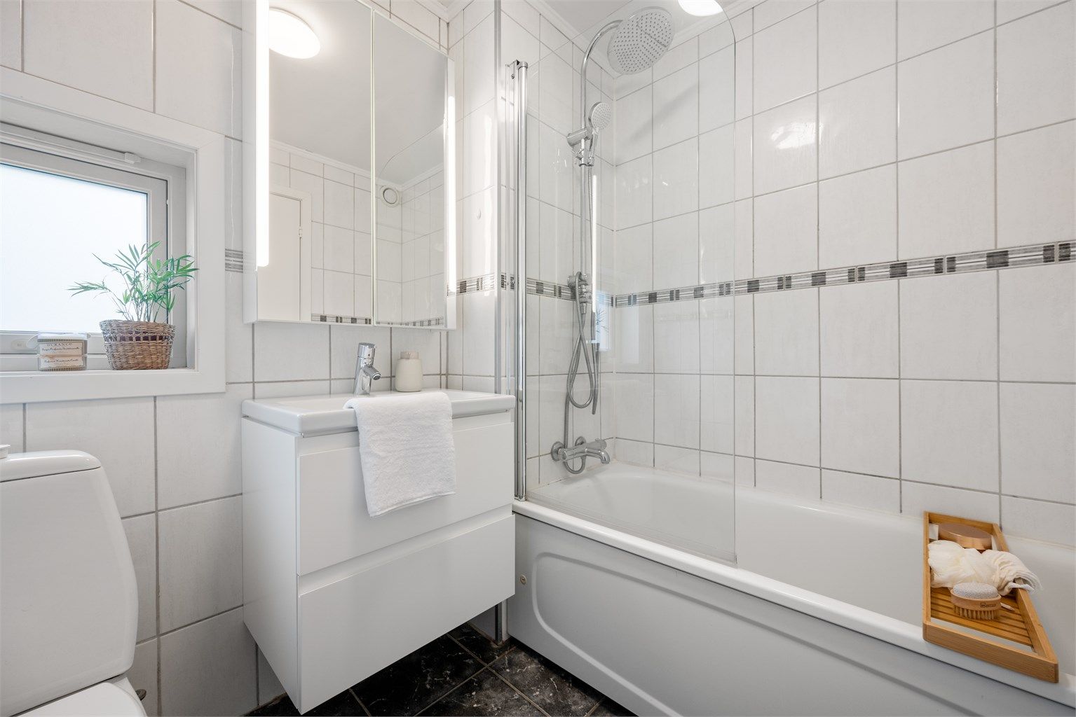 Servant med oppbevaring i skuffer, speil på vegg, toalett og badekar med dusj. 