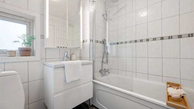 Servant med oppbevaring i skuffer, speil på vegg, toalett og badekar med dusj.