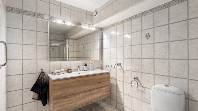 Vegger og gulv er flislagt med gulvvarme, badet er videre utstyrt med gulvstående WC, dusj og stort servantmøbel med speil med belysning.