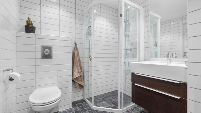 Badet har vegghengt toalett dusjhjørne med skyvedør