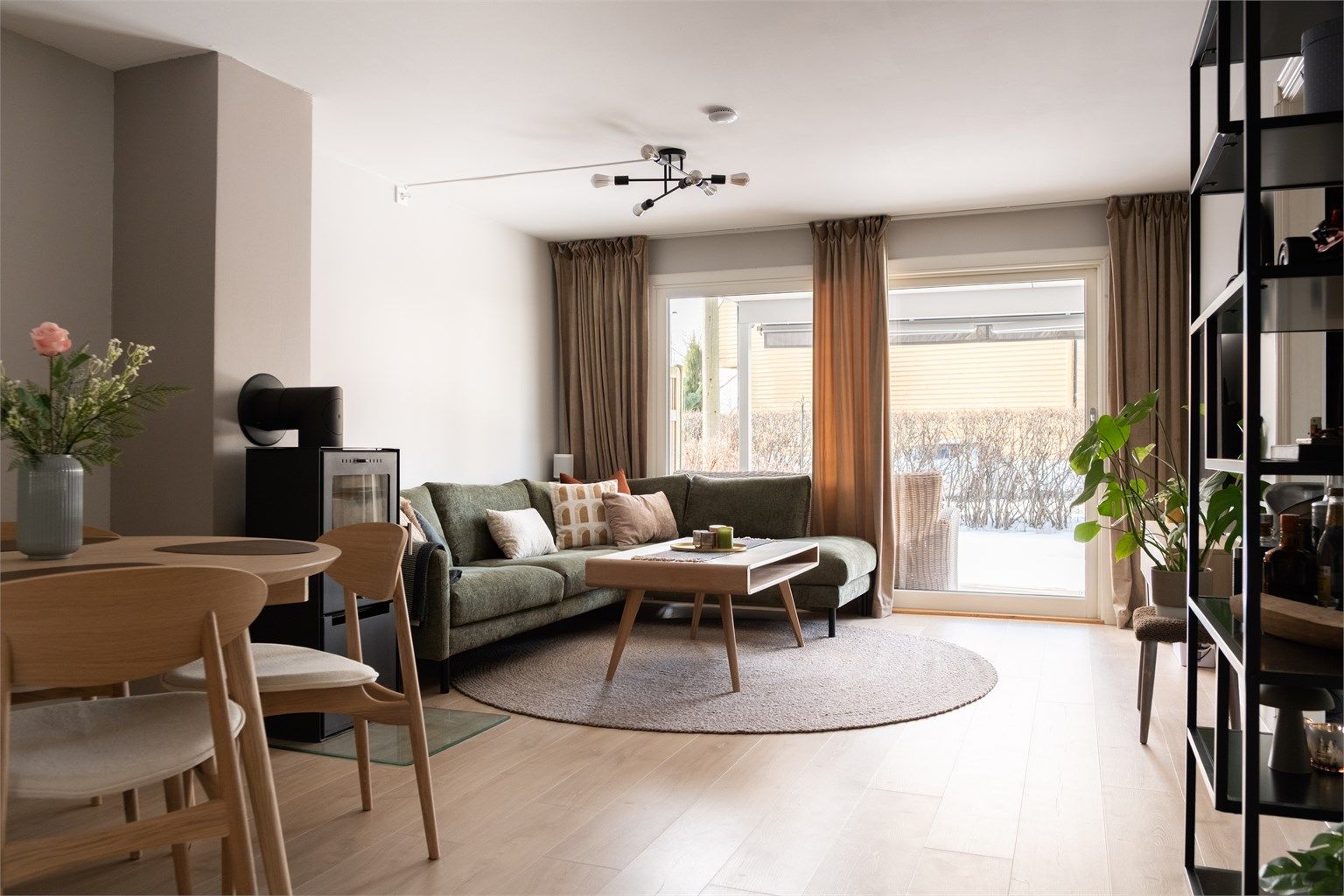 Romslig stue med peisovn som skaper lun atmosfære. Store vinduer slipper inn rikelig med dagslys.