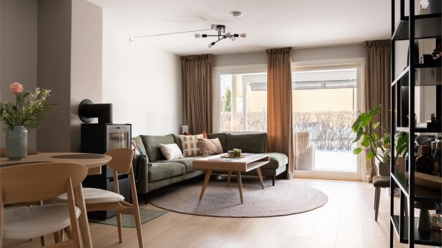 Romslig stue med peisovn som skaper lun atmosfære. Store vinduer slipper inn rikelig med dagslys.