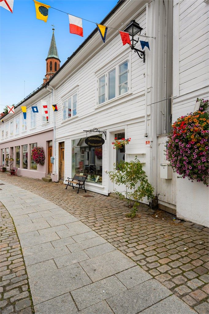 Midt i hjertet av Tvedestrand - Brosteinsbelagte gate med butikker og cafeèr rett utenfor døren.