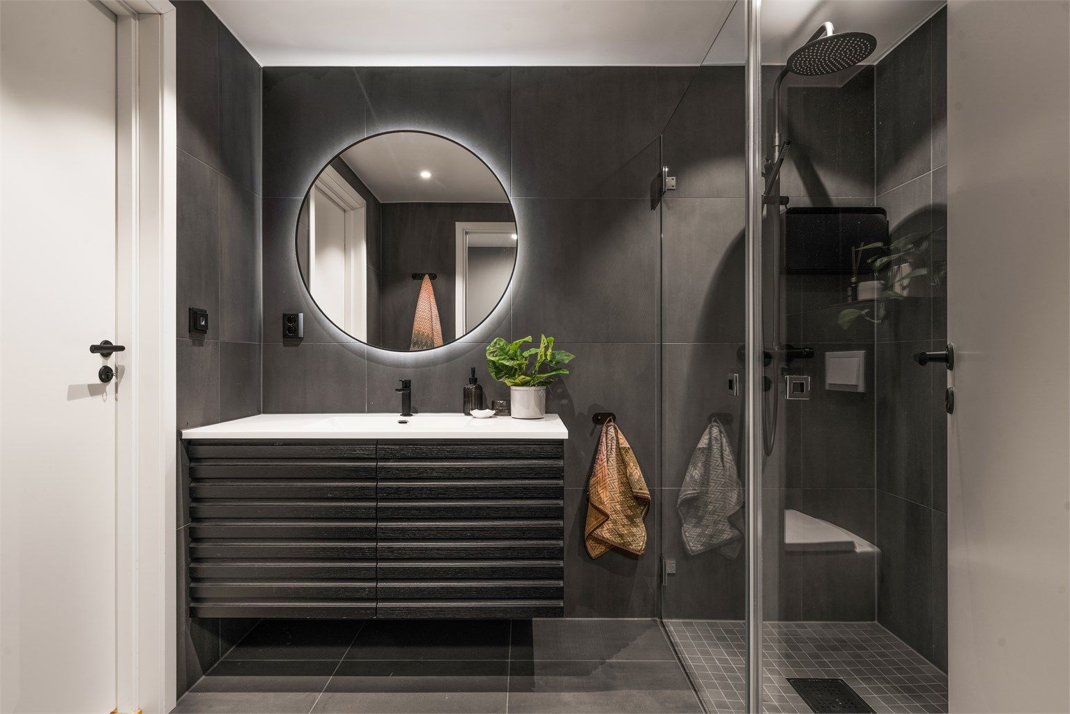 Baderomsinnredningen har god oppbevaringsplass, og det runde speilet har integrert LED-belysning.