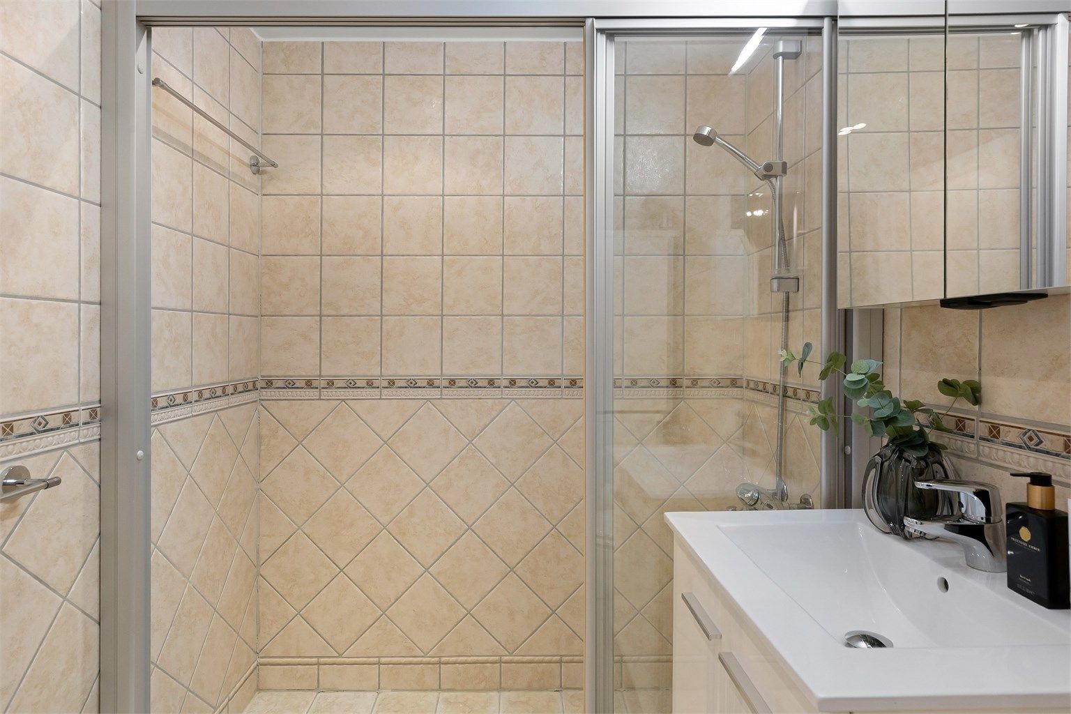 Rommet er utstyrt med dusjhjørne med skyvedører, vegghengt toalett og servantinnredning.