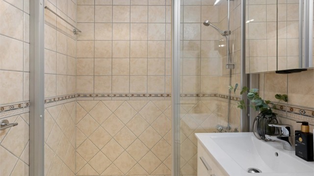 Rommet er utstyrt med dusjhjørne med skyvedører, vegghengt toalett og servantinnredning.