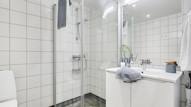 Baderommet har heldekkende servant med underskap og dusjhjørne i glass.