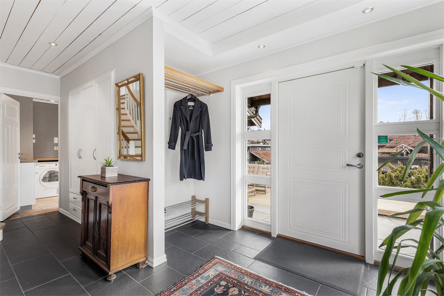 Romslig, flislagt entré med plass til oppbevaring av ytterklær og sko.