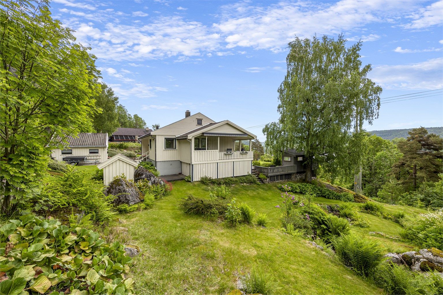 Eiendommen ligger i et svakt skrånende terreng, omkranset av natur og hage.